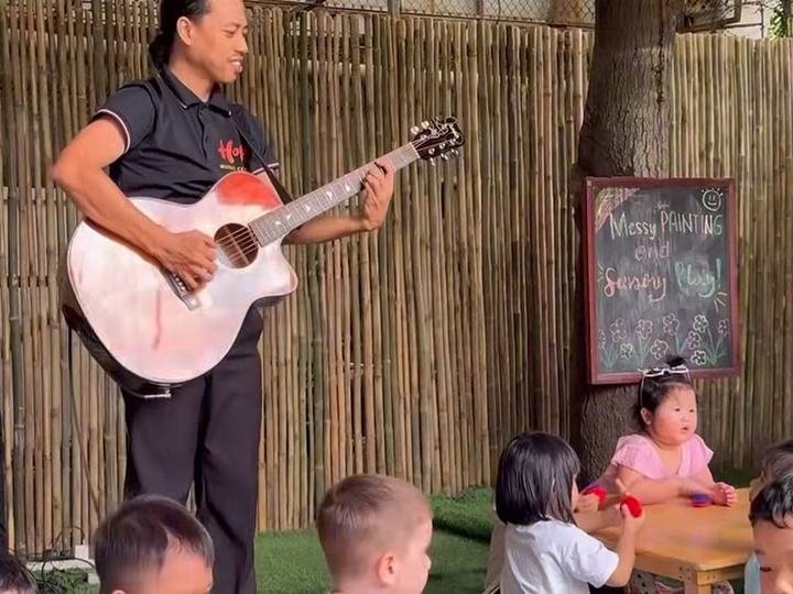 Teacher playing guitar for children seated at a table