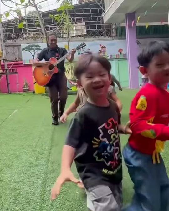 Teacher with a guitar leading children running across the grass